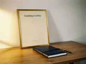 Ingelijst professioneel coachingcertificaat op een eiken bureau met leren notitieboek en pen, warm gouden zijlicht.